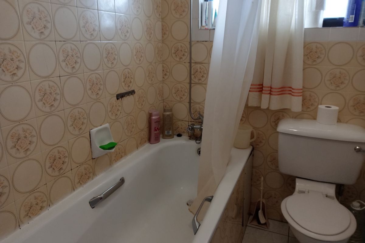 A dated bathroom featuring a standard bathtub with shower attachment, toilet, and vintage floral-patterned wall tiles.