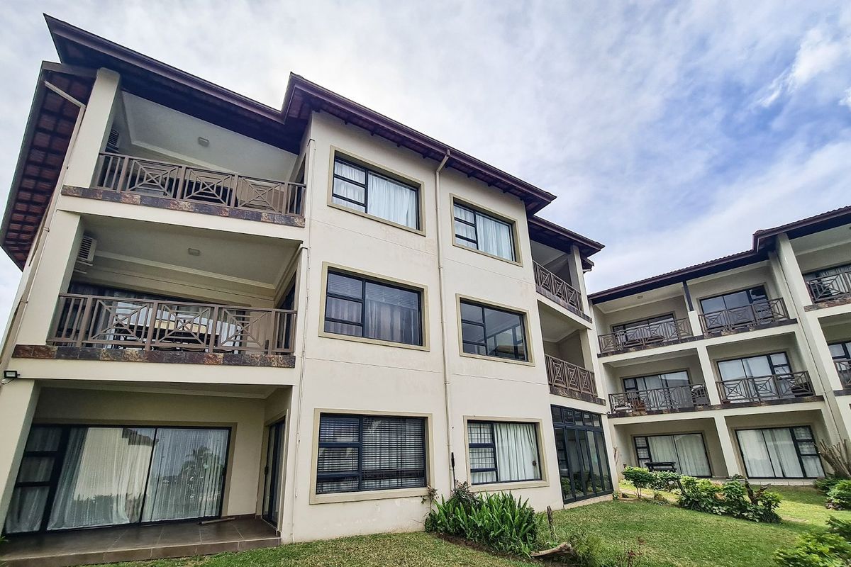 Rear view of a multi-story apartment complex featuring private balconies, sliding glass doors, and well-maintained landscaped garden areas.