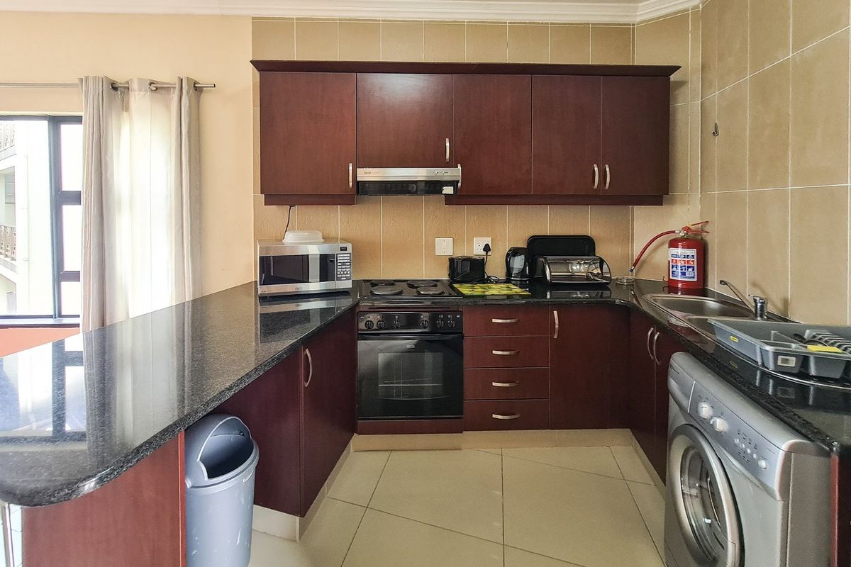 A functional kitchen featuring dark wood cabinetry, granite countertops, built-in oven, electric hob, and tiled splashback with integrated plumbing for a washing machine.
