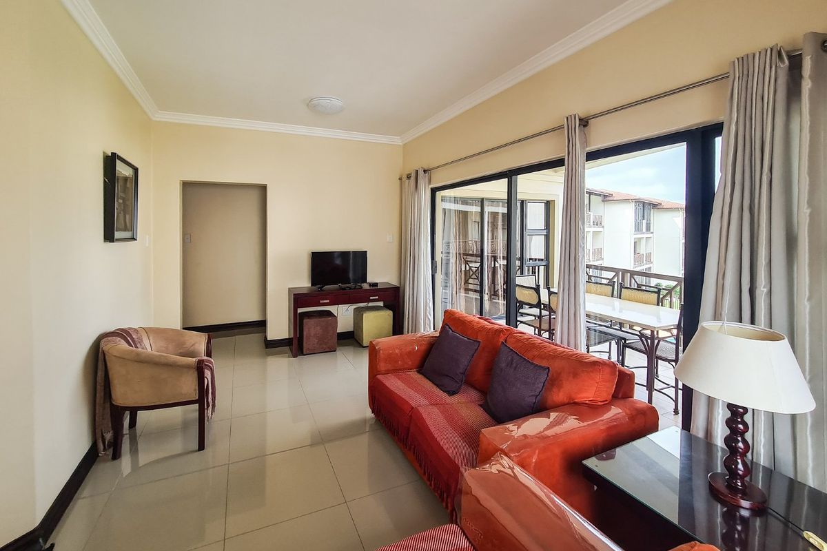 A bright living room featuring large sliding glass doors that open onto a balcony, with neutral tiled flooring and crown molding throughout.