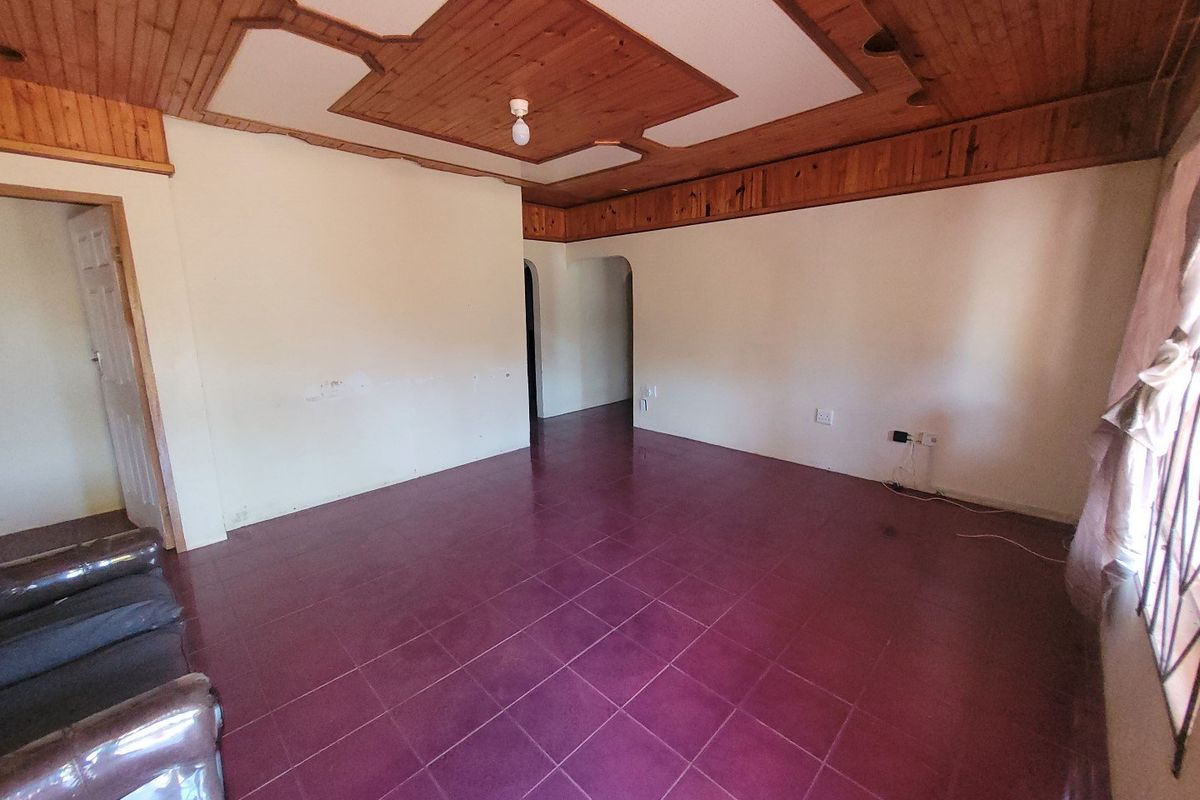 An empty living room featuring a distinctive timber ceiling, ceramic floor tiles, and an arched doorway leading to adjacent areas.