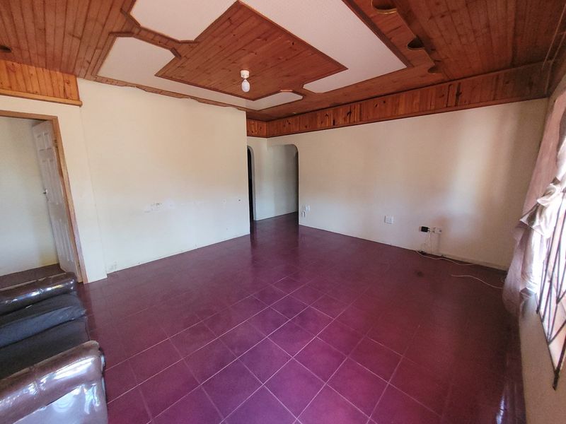 An empty living room featuring a distinctive timber ceiling, ceramic floor tiles, and an arched doorway leading to adjacent areas.