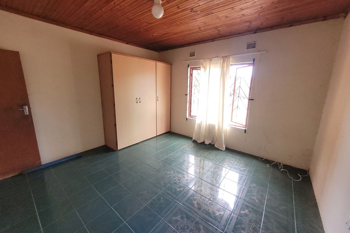 A vacant bedroom featuring tiled flooring, a timber-paneled ceiling, and a built-in wardrobe, offering a blank canvas for renovation.