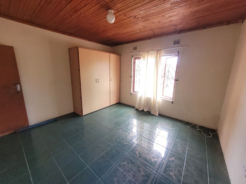 A vacant bedroom featuring tiled flooring, a timber-paneled ceiling, and a built-in wardrobe, offering a blank canvas for renovation.