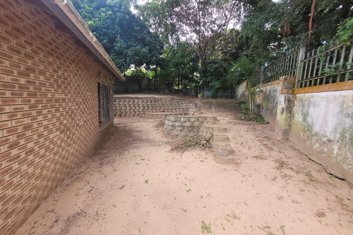 Rear garden area featuring tiered brick retaining walls, perimeter boundary wall with security fencing, and an expansive sandy ground surface.