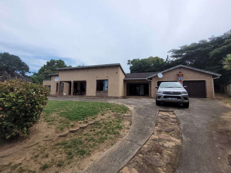 Front view of a single-story house featuring a concrete driveway, double garage, and a covered patio area set within a spacious garden.