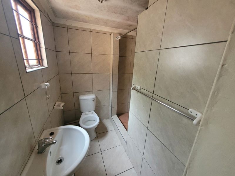 A functional bathroom featuring tiled walls and floors, a pedestal basin, toilet, and a walk-in shower enclosure.