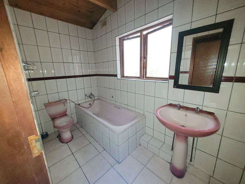 A dated bathroom featuring a pink pedestal basin, matching bathtub and toilet, with full-height wall tiling and a timber-clad ceiling.