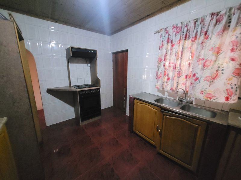 A functional kitchen featuring tiled walls, wooden ceiling, built-in oven with extractor fan, and a double basin sink with wooden cabinetry.