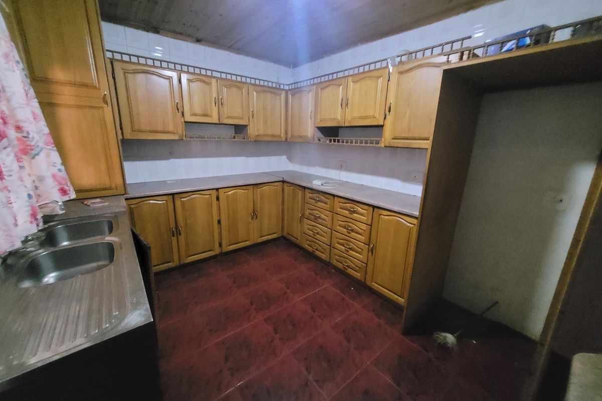A dated kitchen featuring wooden cabinetry, laminate countertops, a double stainless steel sink, and tiled flooring with a timber ceiling.
