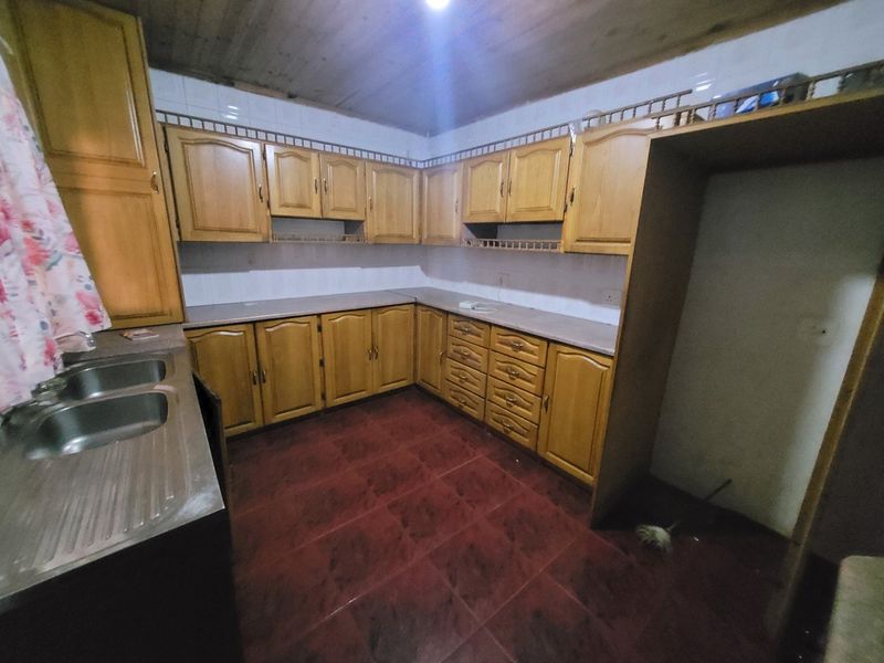 A dated kitchen featuring wooden cabinetry, laminate countertops, a double stainless steel sink, and tiled flooring with a timber ceiling.