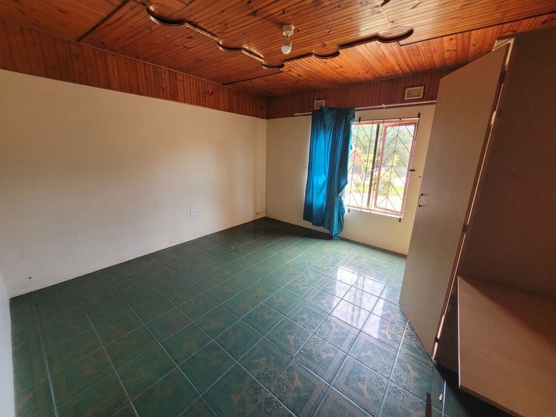 An empty bedroom featuring tiled flooring, a wooden tongue and groove ceiling, and a built-in cupboard with security bars on the window.