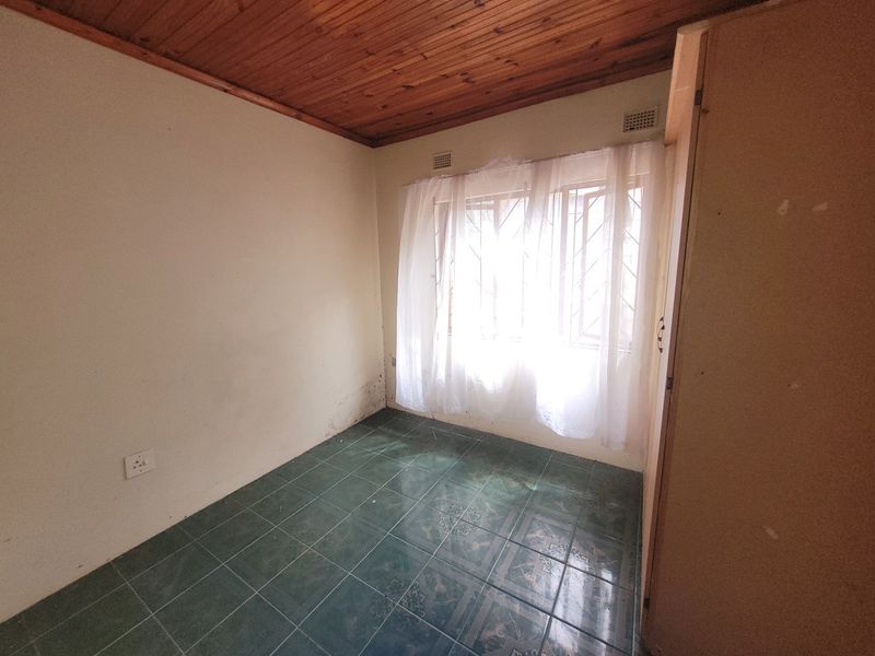 An empty bedroom featuring a timber ceiling, tiled flooring, and a built-in cupboard, with security bars installed on the window.