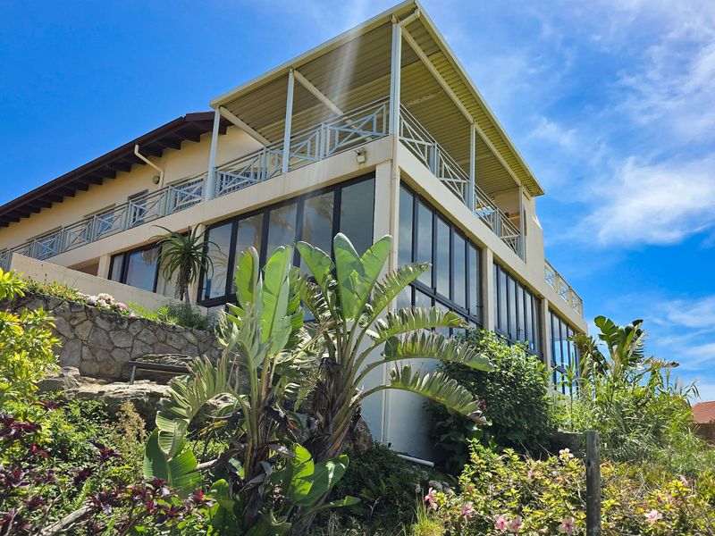 Rear elevation of the apartment building featuring a large covered balcony, extensive glass sliding doors, and a landscaped stone retaining wall.