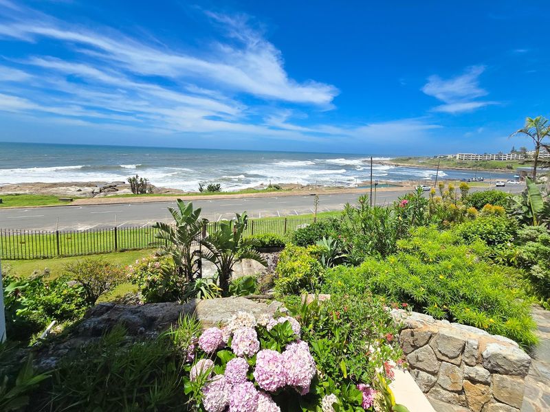 A scenic coastal view overlooking the ocean, featuring a landscaped garden with stone retaining walls and a clear view of the shoreline.