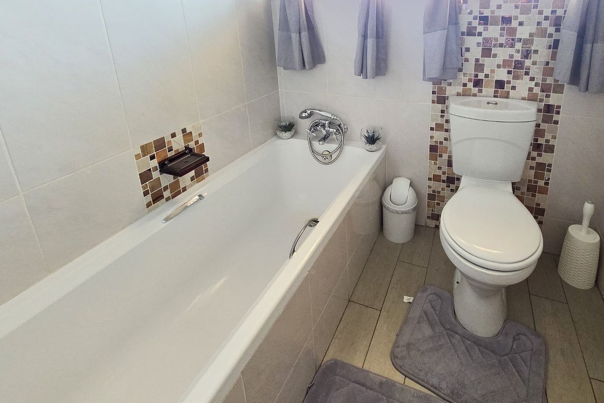 A functional bathroom featuring a bathtub with chrome mixer tap, a standard toilet, and decorative mosaic tile accents on the walls.