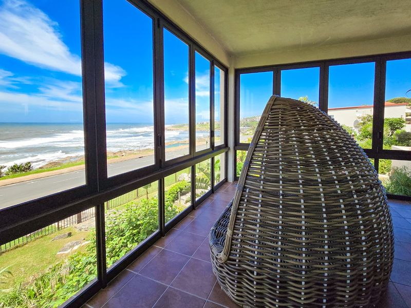 Enclosed balcony featuring tiled flooring and expansive aluminium-framed windows offering panoramic ocean and coastal views.