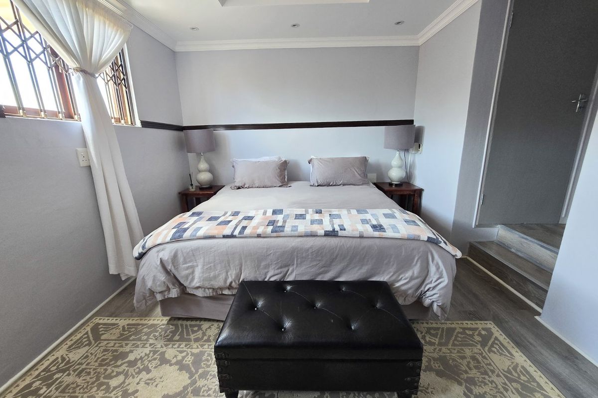 A well-maintained bedroom featuring laminate flooring, recessed ceiling detail, and secure window treatments, offering a comfortable and neutral living space.