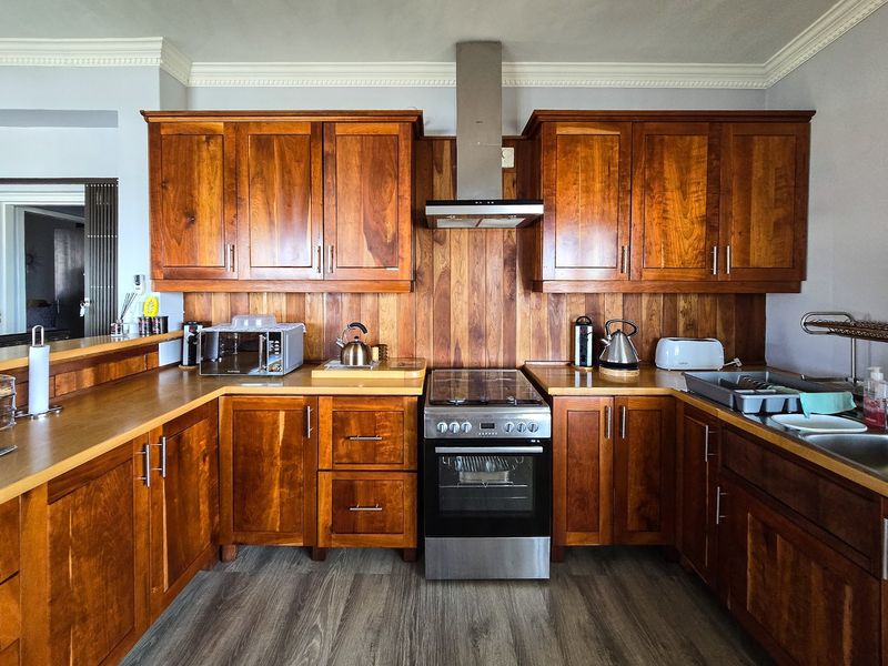 A well-maintained kitchen featuring warm wooden cabinetry, matching timber splashbacks, stainless steel appliances, and modern laminate flooring with classic crown molding details.