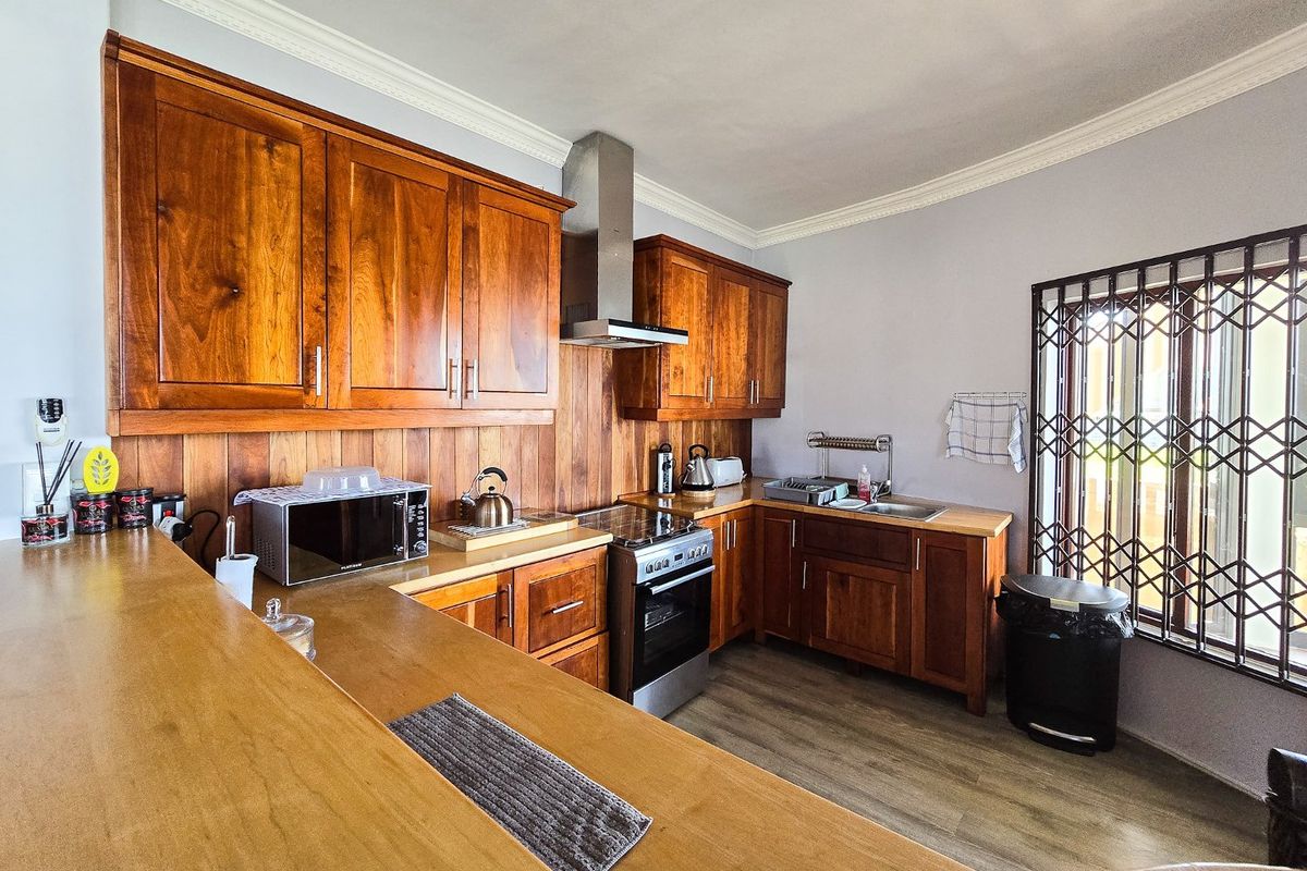 A functional kitchen featuring warm-toned wooden cabinetry, a matching wooden backsplash, stainless steel appliances, and durable laminate flooring.
