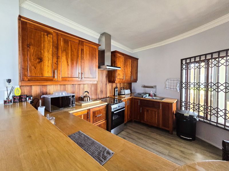 A functional kitchen featuring warm-toned wooden cabinetry, a matching wooden backsplash, stainless steel appliances, and durable laminate flooring.