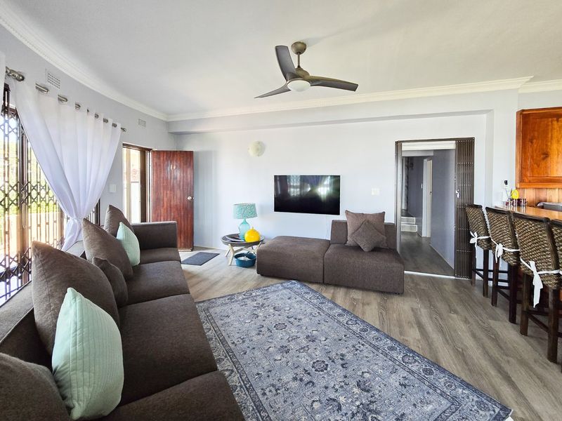 Open plan living area featuring laminate flooring, a ceiling fan, and a breakfast bar connecting to the kitchen space.