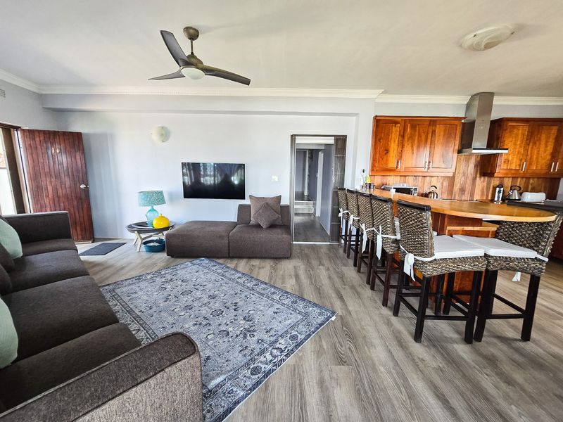 Open-plan living and kitchen area featuring laminate flooring, a breakfast bar with wooden cabinetry, and a ceiling fan.