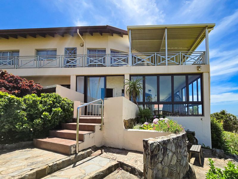 Rear elevation of the apartment featuring a covered balcony with metal balustrades, stone retaining walls, and a tiled staircase leading to the main entrance.