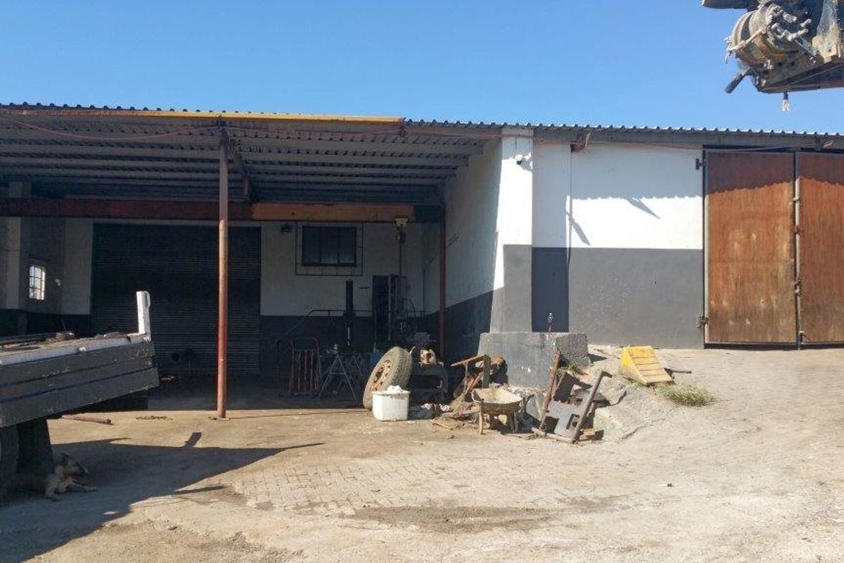 Industrial property exterior featuring a covered loading area, roller shutter door, and double timber access doors with a concrete yard.