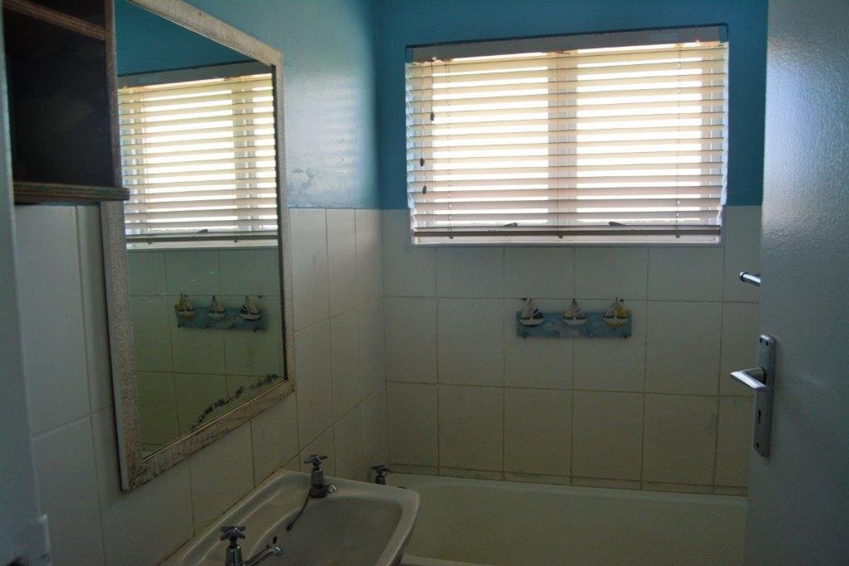 A functional bathroom featuring a bathtub, pedestal basin, and tiled splashback, currently requiring cosmetic updates to modernize the space.