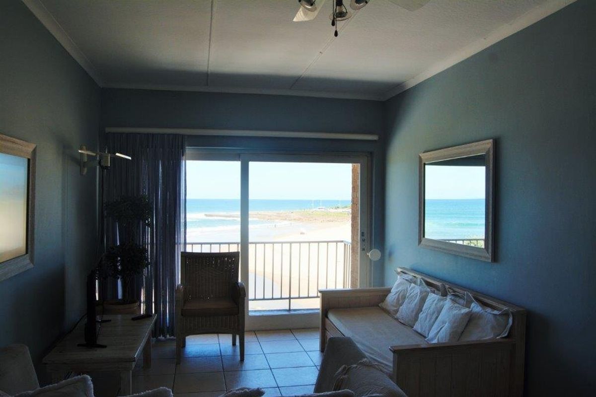 A living room featuring tiled floors, a ceiling fan, and a sliding glass door that opens onto a balcony with ocean views.