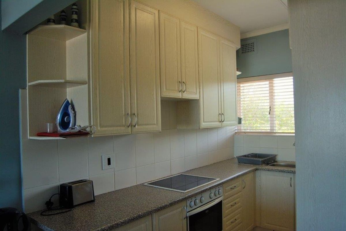 A functional kitchen featuring light-toned laminate cabinetry, a tiled backsplash, built-in oven, electric hob, and a stainless steel sink with natural light.