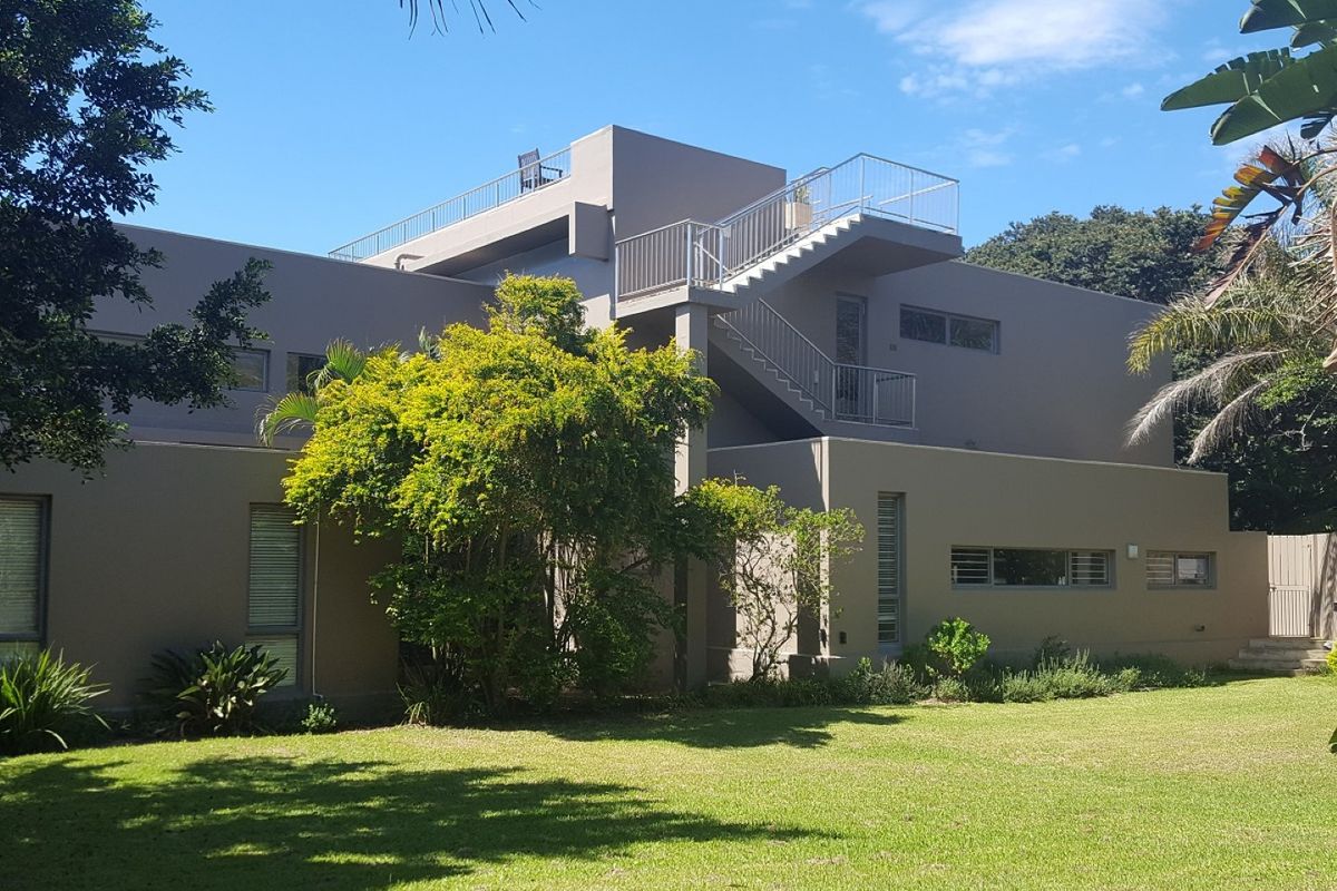 Rear view of a modern multi-story house featuring an external staircase leading to an upper-level balcony and a well-maintained garden.