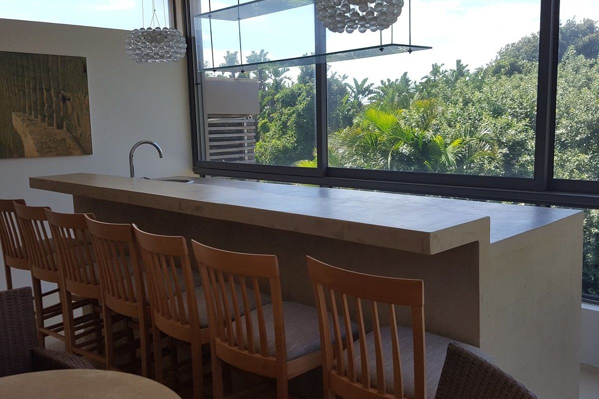 Modern kitchen area featuring a built-in concrete breakfast bar with integrated sink and large windows offering scenic garden views.