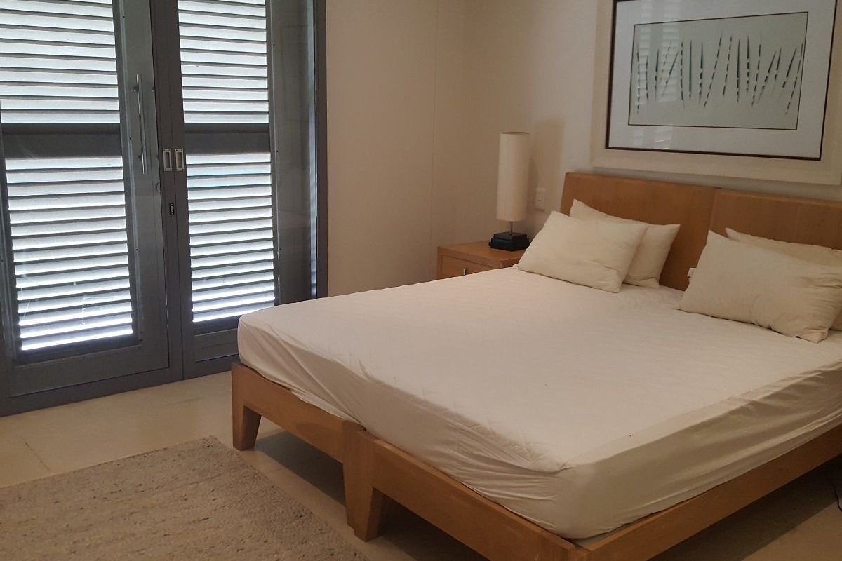 A well-maintained bedroom featuring neutral tones, tiled flooring, and large louvre shutter doors providing access to the exterior.