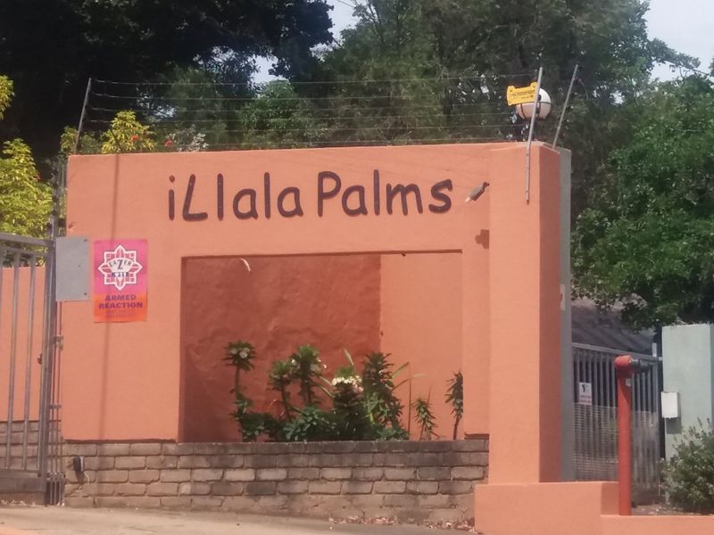 Entrance view of the iLala Palms residential complex featuring a masonry boundary wall, security gate, and electric fencing.