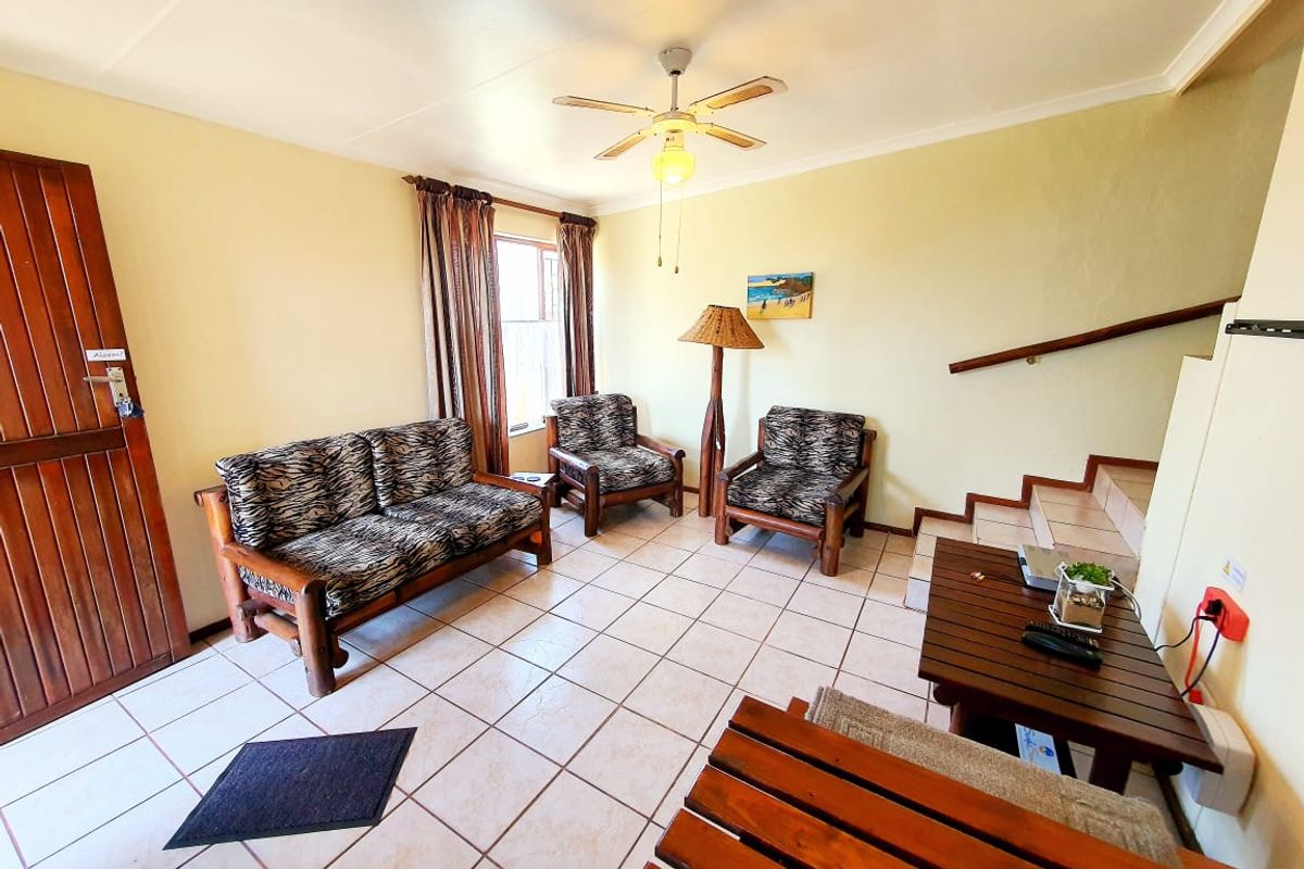 A living room area featuring tiled flooring, a ceiling fan, and a staircase with a wooden handrail.
