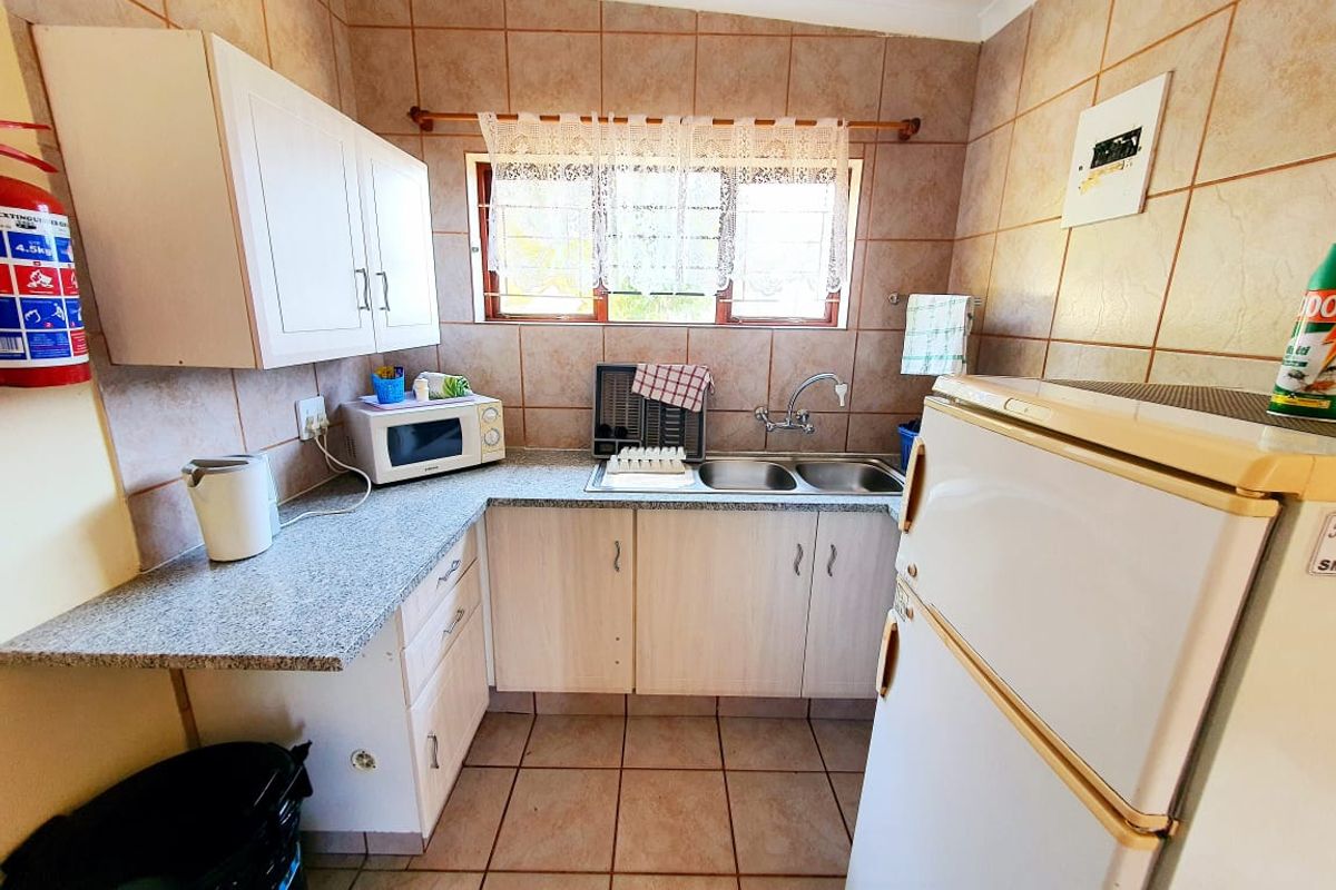 A functional kitchen featuring tiled walls and flooring, laminate countertops, double basin sink, and built-in cabinetry.