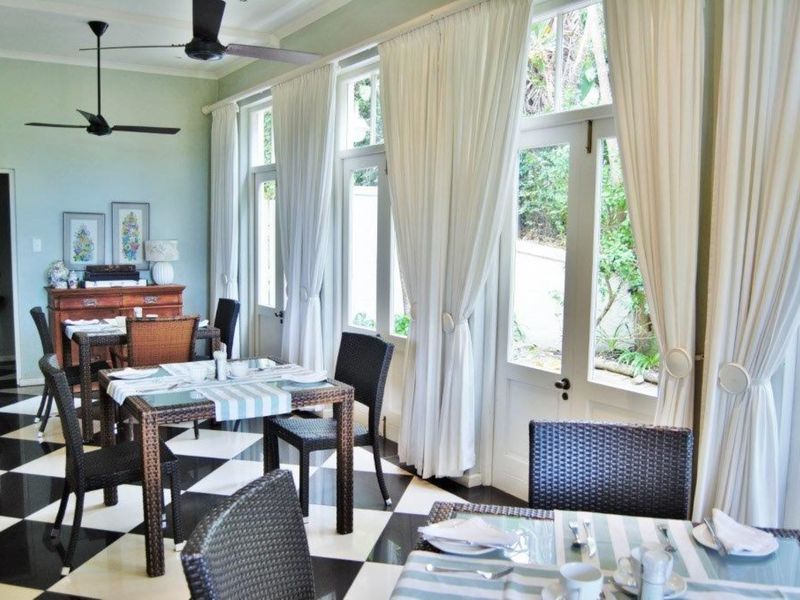 A bright dining area featuring classic black and white checkered flooring, ceiling fans, and large windows with direct access to the garden.
