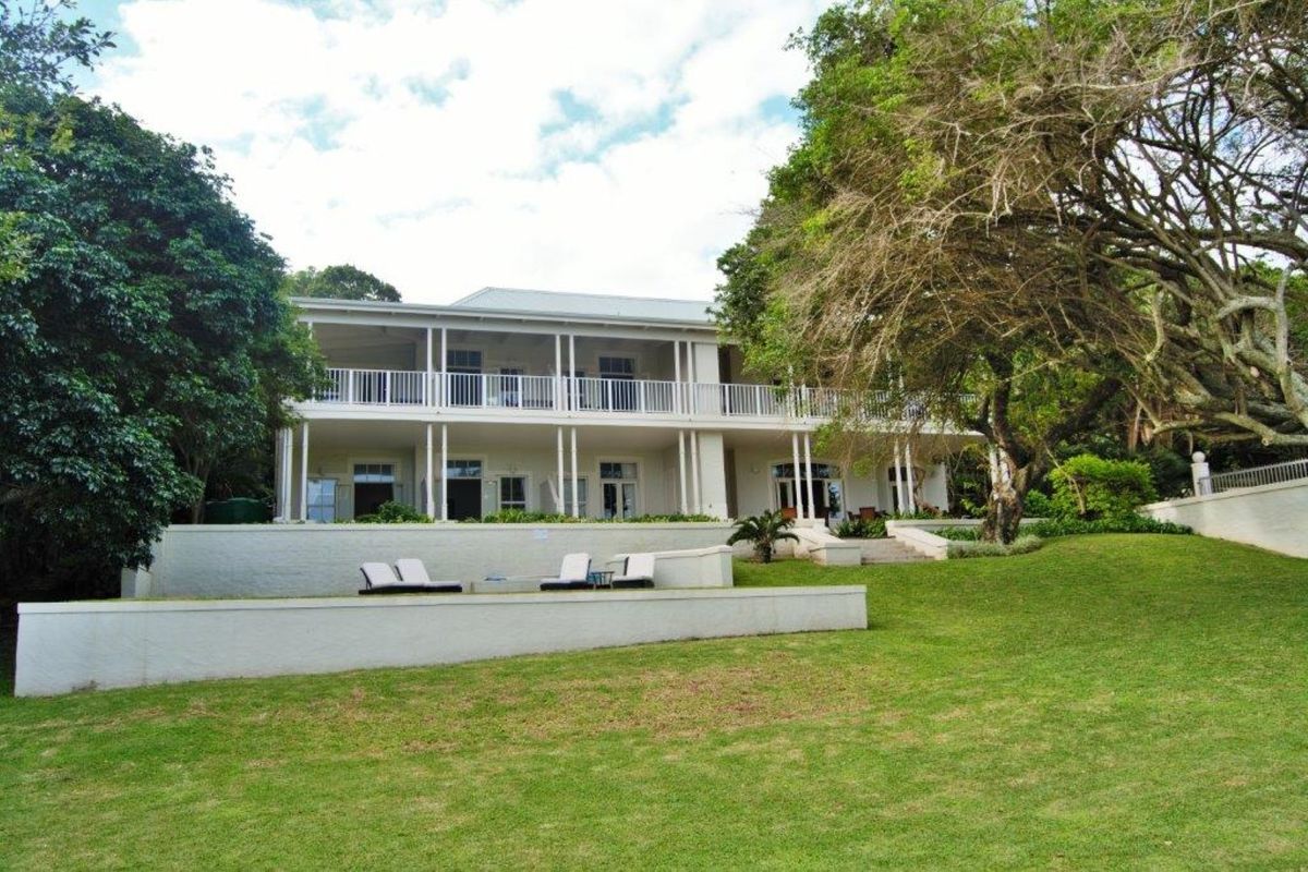 A spacious rear view of a two-story commercial property featuring a large veranda, retaining walls, and a well-maintained garden area.
