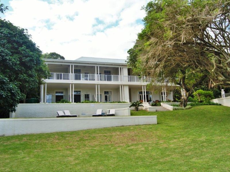 A spacious rear view of a two-story commercial property featuring a large veranda, retaining walls, and a well-maintained garden area.