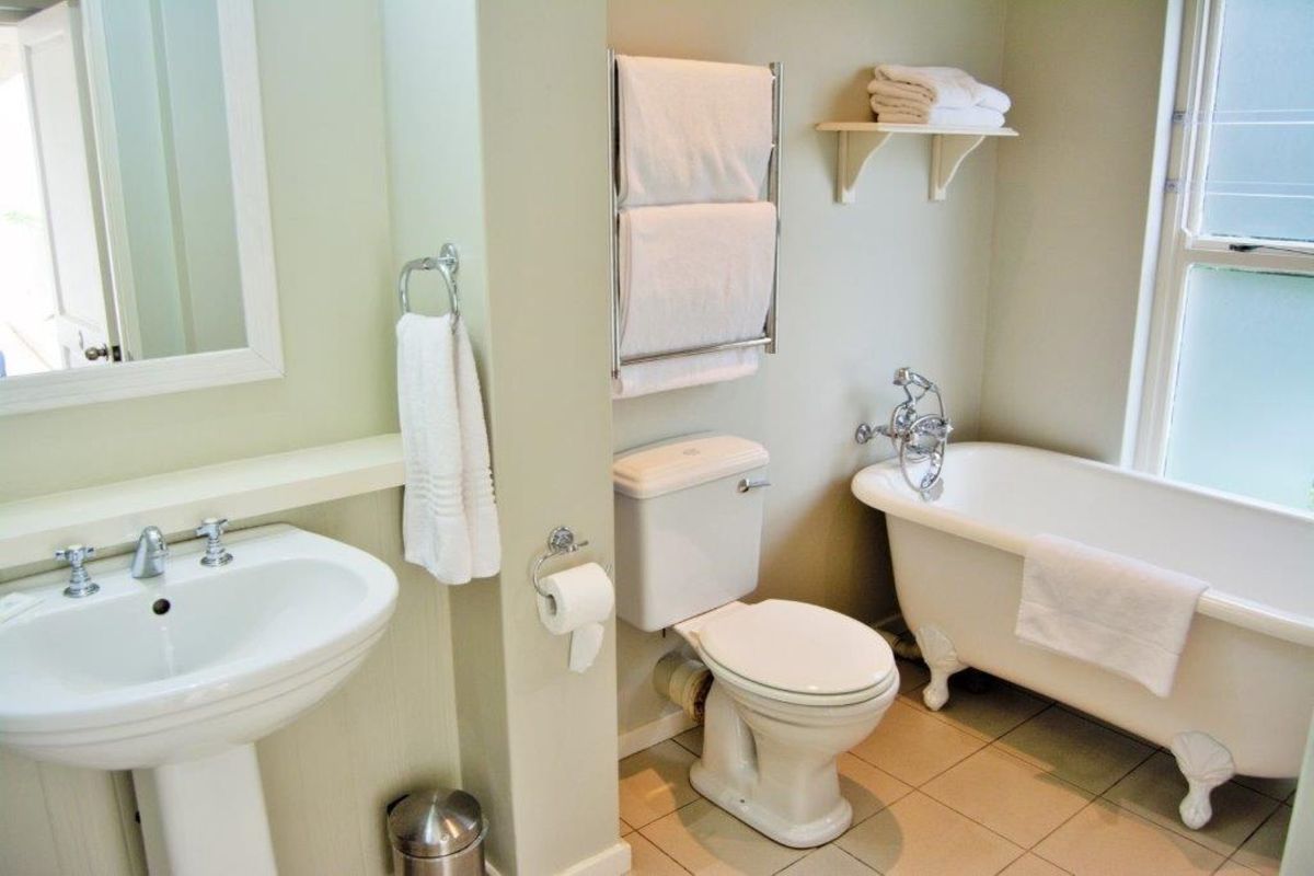 A well-maintained bathroom featuring a classic clawfoot bathtub, pedestal sink, toilet, and a heated towel rail with neutral wall finishes.