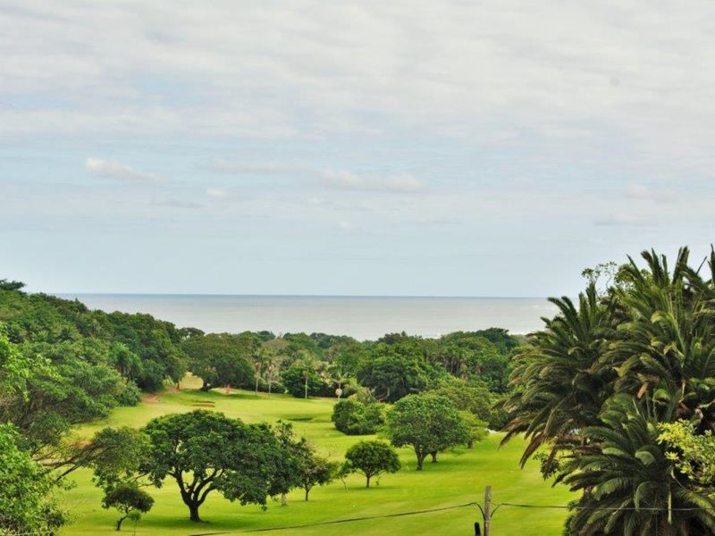 A scenic elevated view overlooking a lush green golf course with the ocean visible in the distance.