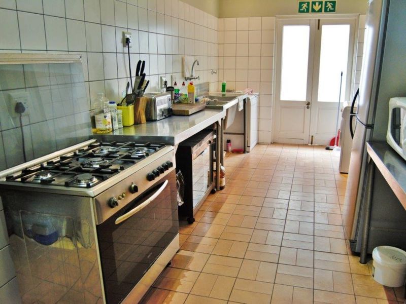 A functional commercial kitchen featuring a gas stove, stainless steel countertops, double sink, and tiled finishes with direct access to the exterior.