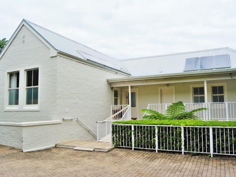 Front exterior view of a commercial building featuring a paved driveway, ramp access, white painted masonry walls, and a metal roof with solar panels.