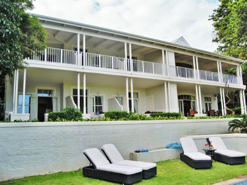 Rear view of a two-story commercial building featuring a spacious veranda with white railings, overlooking a landscaped garden and pool area.