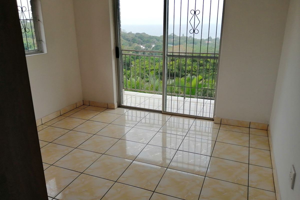 An empty bedroom featuring tiled flooring, a sliding glass door with security gate, and access to a balcony with scenic views.
