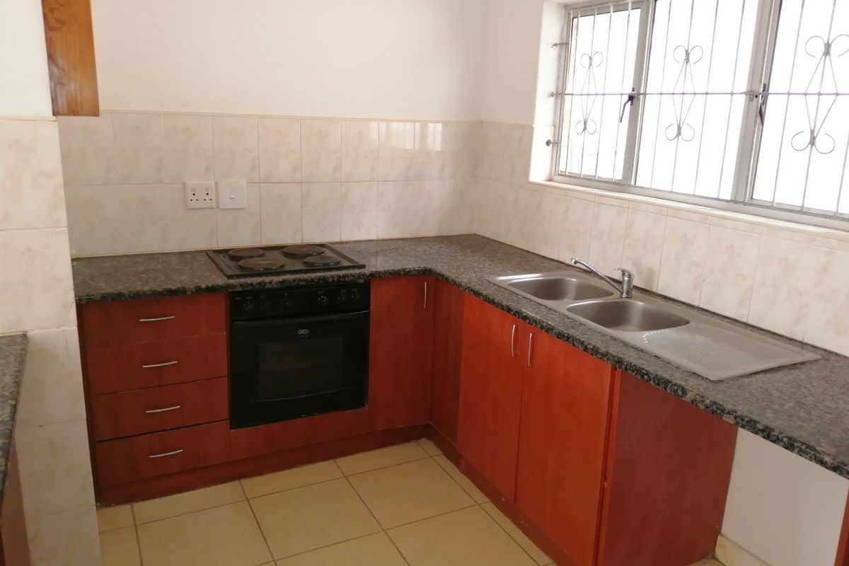 A functional kitchen featuring wooden cabinetry, granite countertops, a built-in oven, electric hob, and a double bowl sink with tiled backsplash.