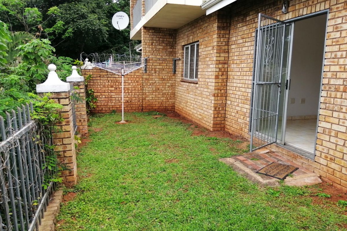 A private rear garden area featuring a face brick facade, a sliding glass door with security gate, and a small lawn.
