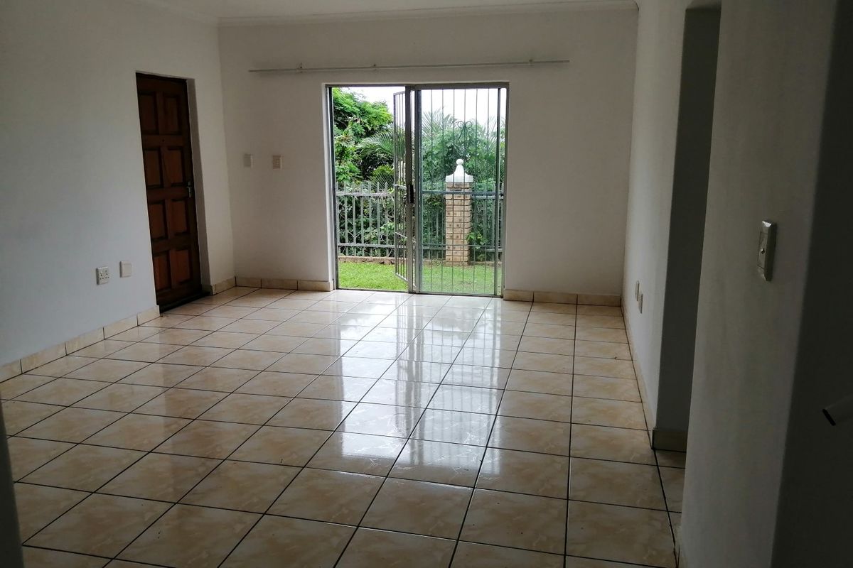 An empty, tiled living area featuring a sliding glass door with a security gate, providing direct access to the garden.